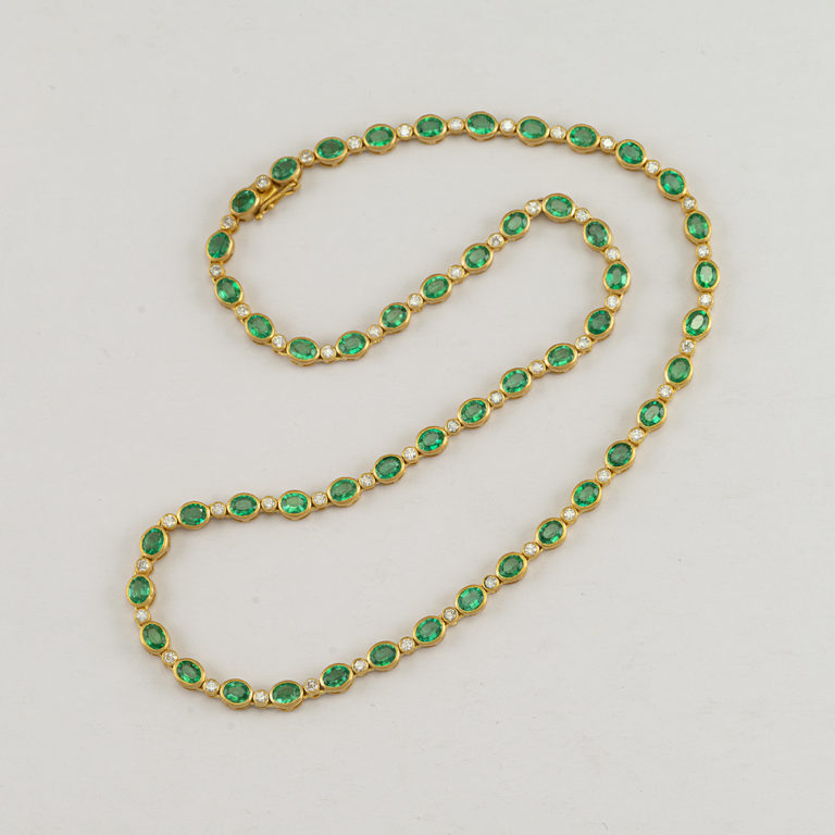 Here is an Emerald necklace that was cast in 14kt yellow gold. Accenting the Emeralds are round, white Diamonds. Both the Diamonds and the Emeralds have been bezel set. The gold has a satin or matte finish. The necklace has a total length of 18".