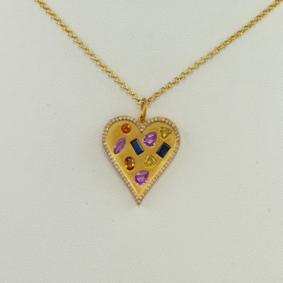 This heart pendant has multi color sapphires and diamonds. Cast in 14kt yellow gold this pendant features 6.66cts of multi color sapphires.