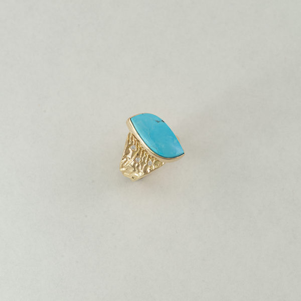 This kingman turquoise ring has diamond accents. Both the diamonds and the kingman turquoise have been set in 14kt yellow gold.