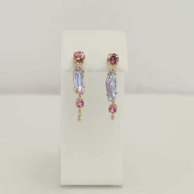 Here are pearl earrings that are one-of-a-kind. The have been accented with pink tourmaline and diamonds. The piece was made using 14kt yellow gold. One pearl is slightly longer than the other. Our designer has added an extra diamond to the shorter pearl to "even" out the length of the earrings.