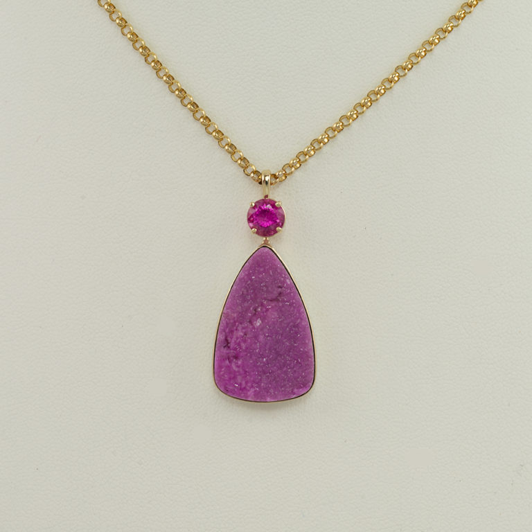 This is a pink druzy tourmaline pendant. The center stone has been accented with a faceted pink tourmaline.