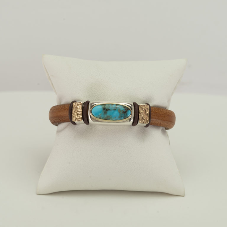 This turquoise and leather bracelet has gold accents. The gold has been reticulated and soldered onto sterling silver "beads". The leather is a tan color and a size 7". The clasp is a magnetic stainless steel. 