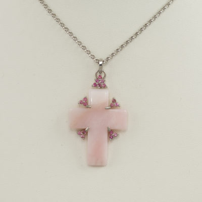 This pink cross pendant was set in sterling silver. The silver has been rhodium plated to prevent tarnishing. The cross has pink tourmaline accents. The cross is Peruvian pink opal. Available with a sterling silver chain or a white gold chain that is sold separately. This piece is one-of-a-kind.