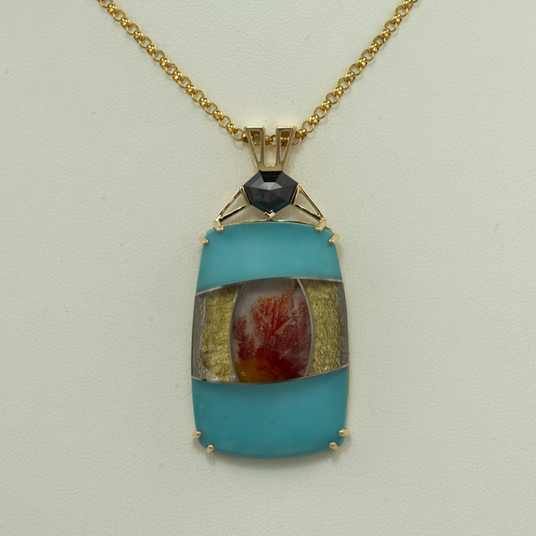 This intarsia pendant features turquoise, quartz, orange oxide, gold foil on black onyx. The pendant has been set in 14kt yellow gold.