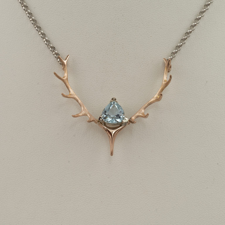 This Aquamarine and antler necklace has a combination of 14kt rose and white gold. The antlers are rose gold and the chain is white gold. The Aquamarine is a trillion cut. The chain has a lobster claw clasp.