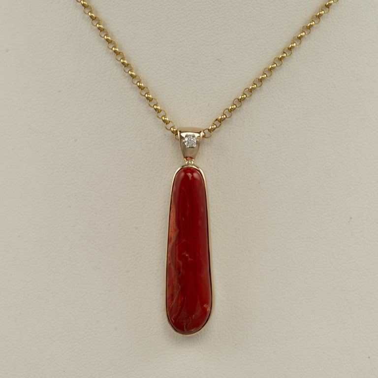 This coral pendant has a diamond accent. Both the diamond and the coral have been set in 14kt yellow gold with a sterling silver backplate. The chain is not included in the price.