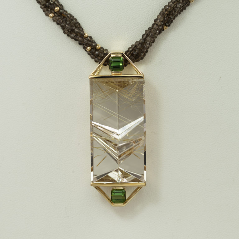 This rutilated quartz pendant was designed by Dan Harrison. The rutilated quartz was cut by Lew Wackler. This is known as a fantasy cut.