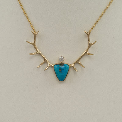 Here is a Kingman Turquoise and antler pendant. It has a diamond accent. Both the diamond and the turquoise have been set in 14kt yellow gold. The chain is included in the price and it has a lobster claw clasp.