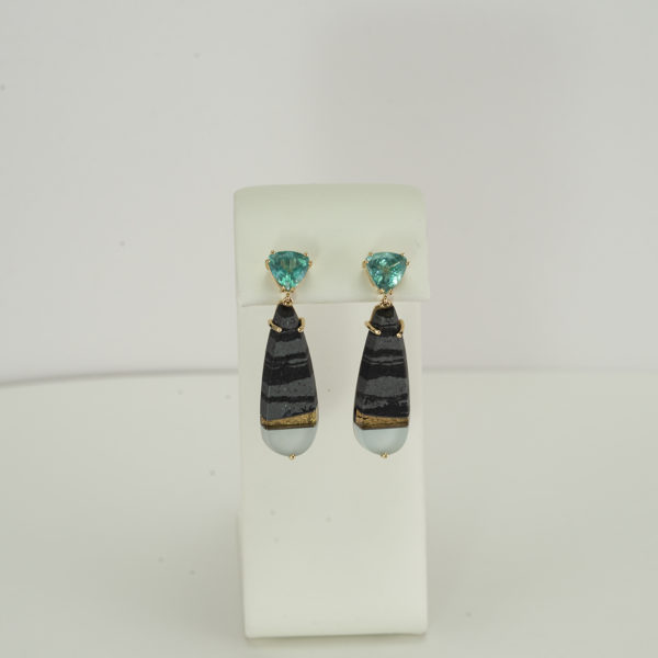 This is the only pair of intarsia earrings in the gallery. The intarsia was made by Steven Walters. The intarsia was made using zebra stone, gold foil, black jade, frosted quartz, and mother of pearl. The earrings were designed by Dan Harrison. The apatite stone have been cut into trillions. The apatite and the intarsia have been set in 14kt yellow gold. We have a pendant to match and you can view it here.