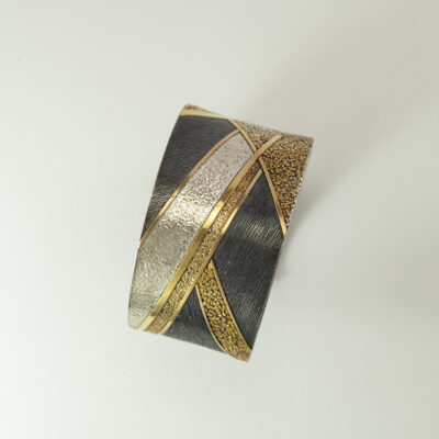 This contemporary cuff was created by Wolfgang Vaatz. It incorporates sterling silver, argentium silver, and 18kt yellow gold. Shown in a size M/L.