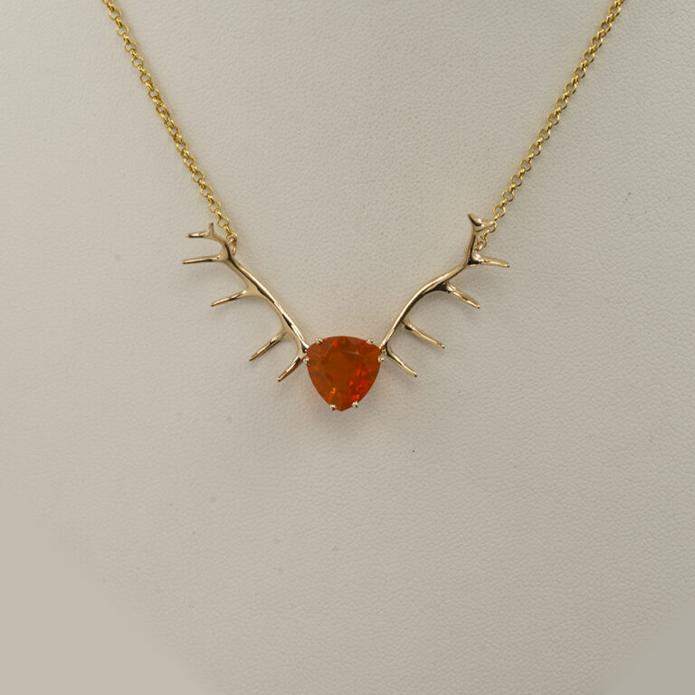 This fire opal and antler pendant has been made with yellow gold. The gold is 14kt and the fire opal has been cut into a trillion.