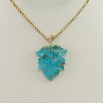 Here is a carved turquoise leaf pendant. It has been set in 14kt yellow gold. The bail has been decorated with round, white diamonds.