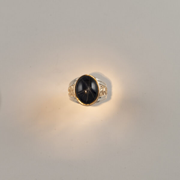 This black star sapphire men's ring is in two tone. The star sapphire was bezel set in 14kt gold. Shown in a size 10.75, but can be re-sized.