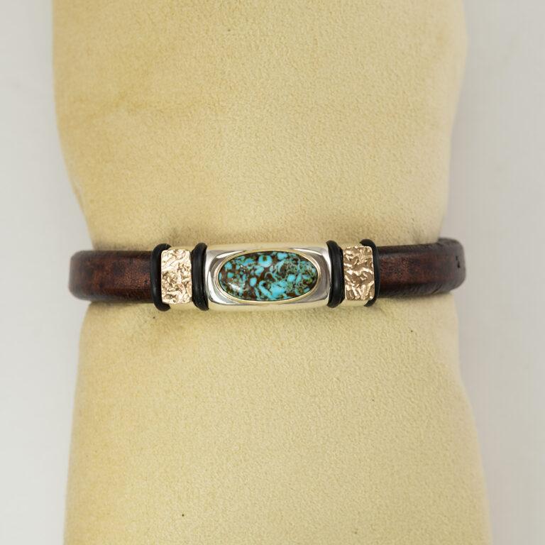This is a leather and turquoise bracelet. The turquoise is from the Kingman mine in Arizona. The leather is made from cowhide. The clasp is a magnetic, stainless steel. Accenting the turquoise are 14kt yellow gold accents. Shown in a size 8.5".