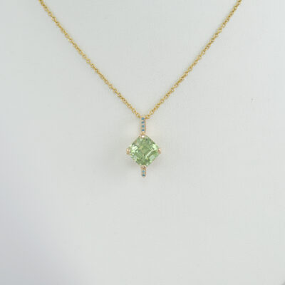 Here is a light green tourmaline pendant. It has blue diamond accents. Both the diamonds and light green tourmaline have been set in 14kt yellow gold.